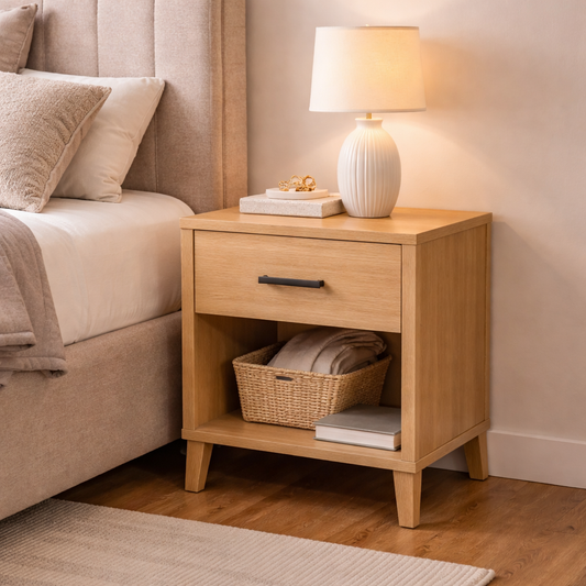 Wooden nightstand with a lamp and books next to a bed in a bedroom.